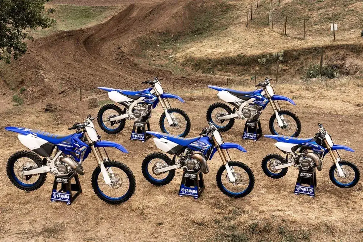 Cinco motocicletas Yamaha de motocross azules y blancas listas para la acción en una pista de tierra.