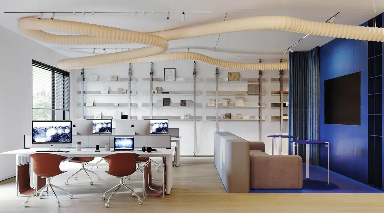 Aménagement de locaux professionnels : bureaux modernes avec postes de travail, étagères remplies de livres et un espace détente bleu vif.