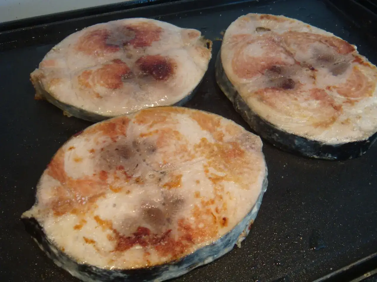 Tres bonito rodajas de pescado en una plancha, dor&aacute;ndose.