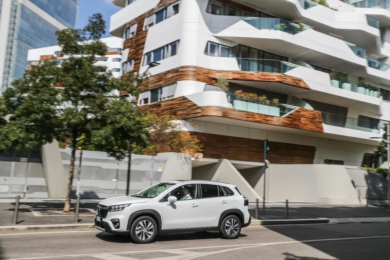 Guida un'auto ibrida bianca in citt&agrave;, con un edificio moderno sullo sfondo. Impara come guidare auto ibrida per un viaggio efficiente.