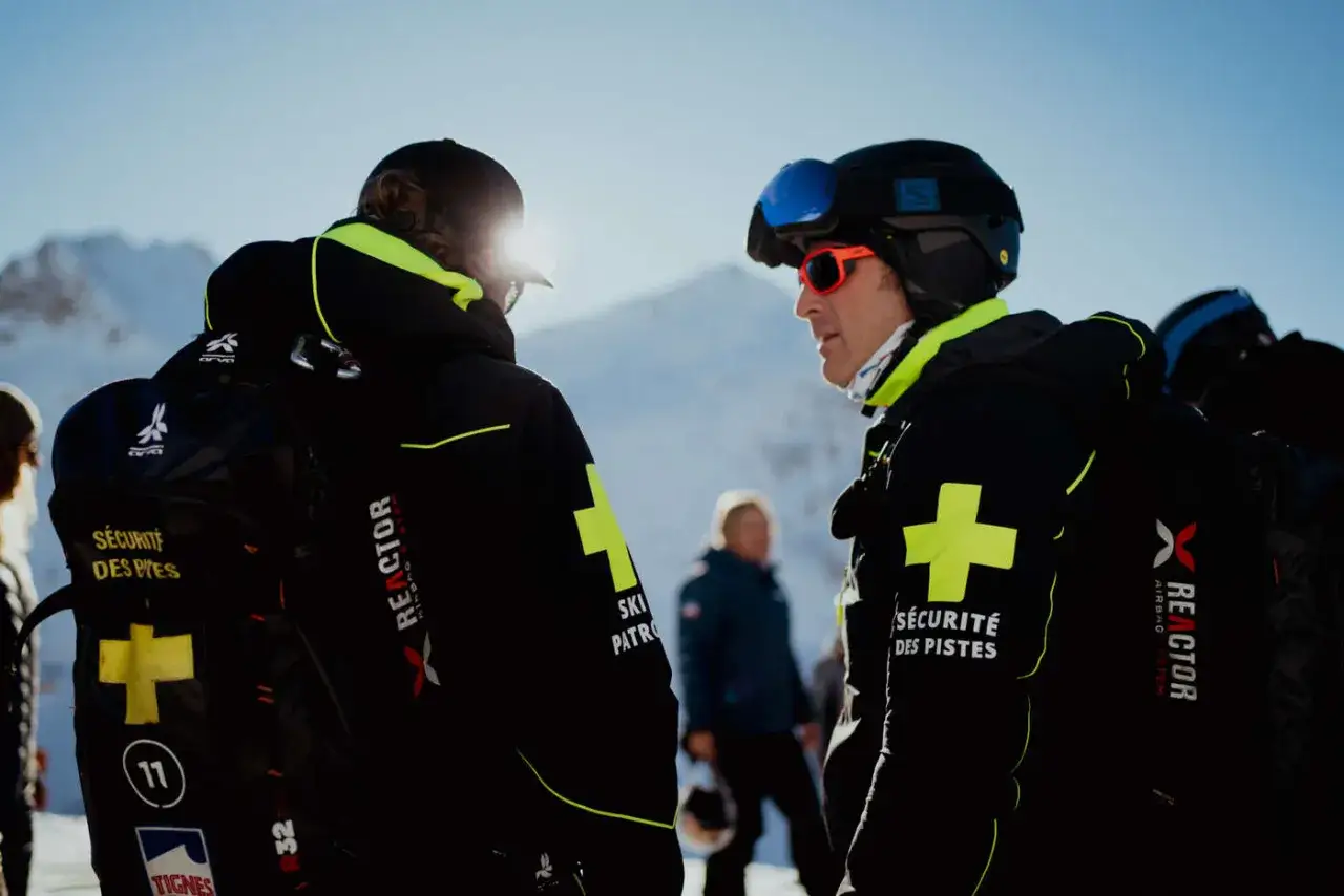Deux pisteurs discutent des règles pour skier en toute sécurité. Leurs vestes portent le logo 