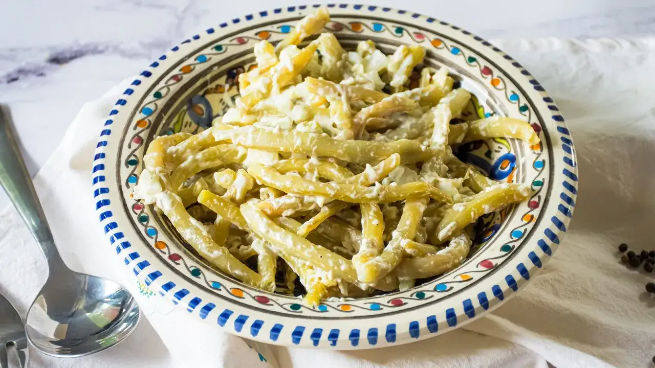 Bohnensalat mit Sahne in einer bunten Schüssel, serviert mit einem Löffel.