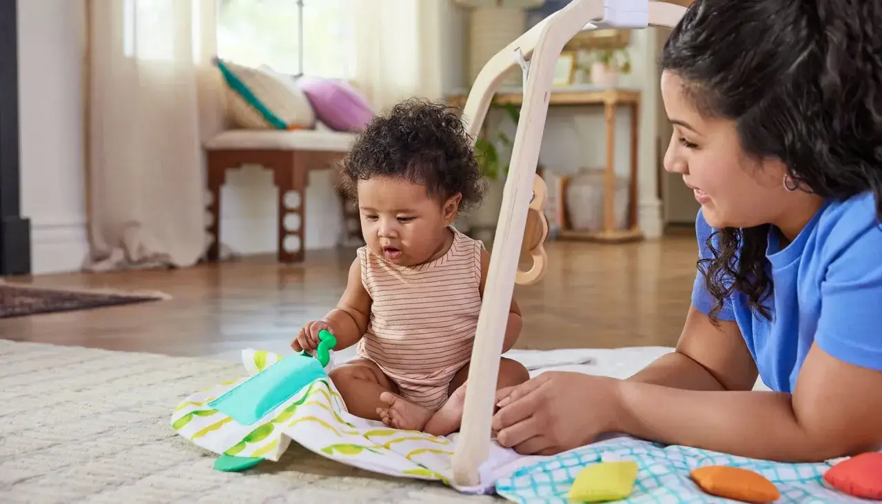 Radosne zabawy z 6 miesięcznym dzieckiem na macie edukacyjnej. Mama czule obserwuje swoje pociechy.