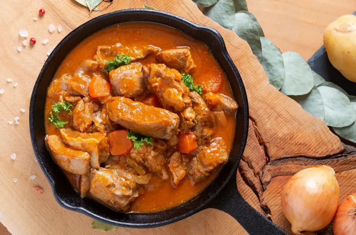 Gulasz z polędwicy wieprzowej w aromatycznym sosie, z kawałkami marchewki i natki pietruszki, podany w żeliwnej patelni.