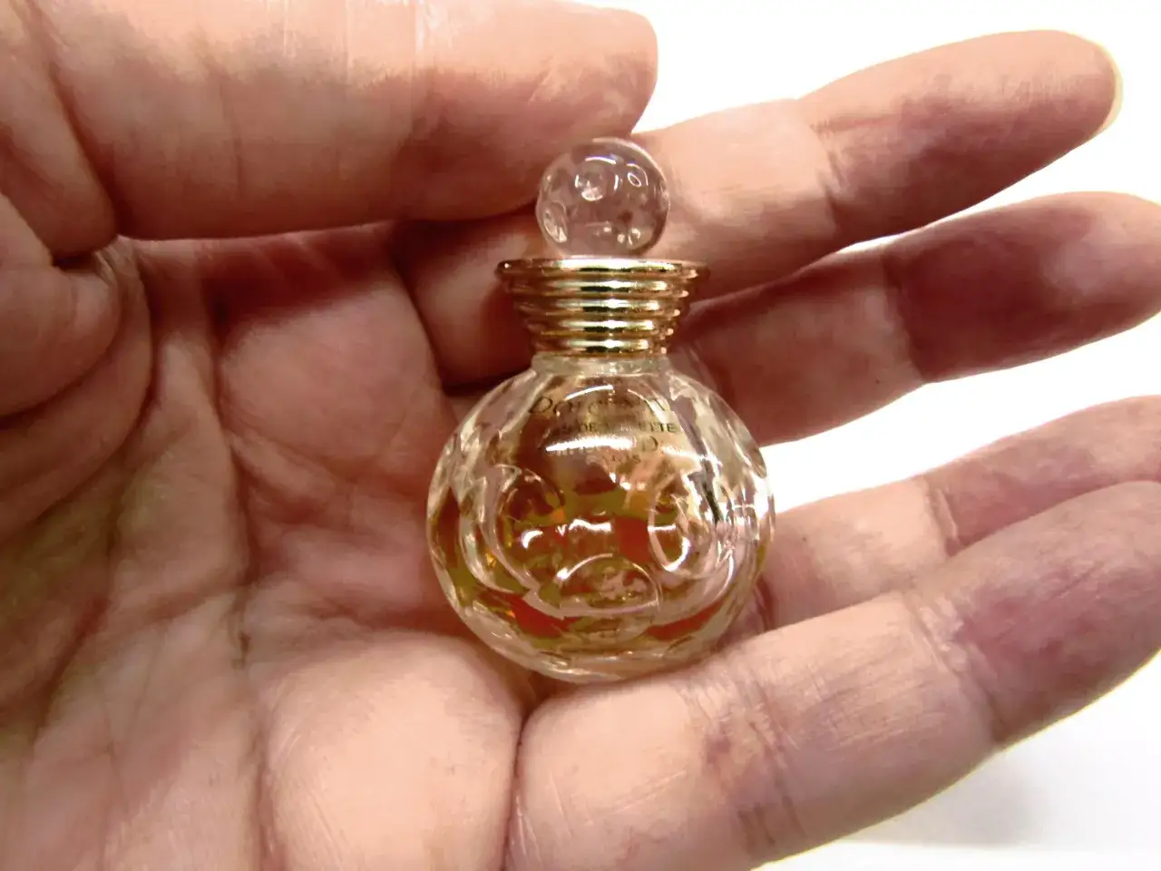 Miniaturowa buteleczka perfum Dior Dolce Vita w dłoni, złoty korek i szkło z wytłoczeniami.
