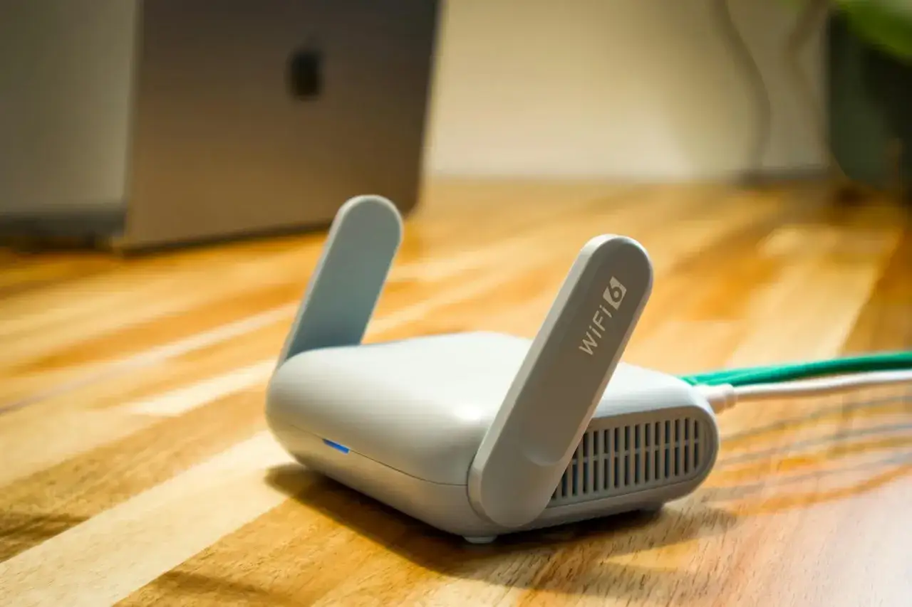 Router Wi-Fi 6 na drewnianym blacie, gotowy do zapewnienia najlepszego internetu. W tle widać laptopa.
