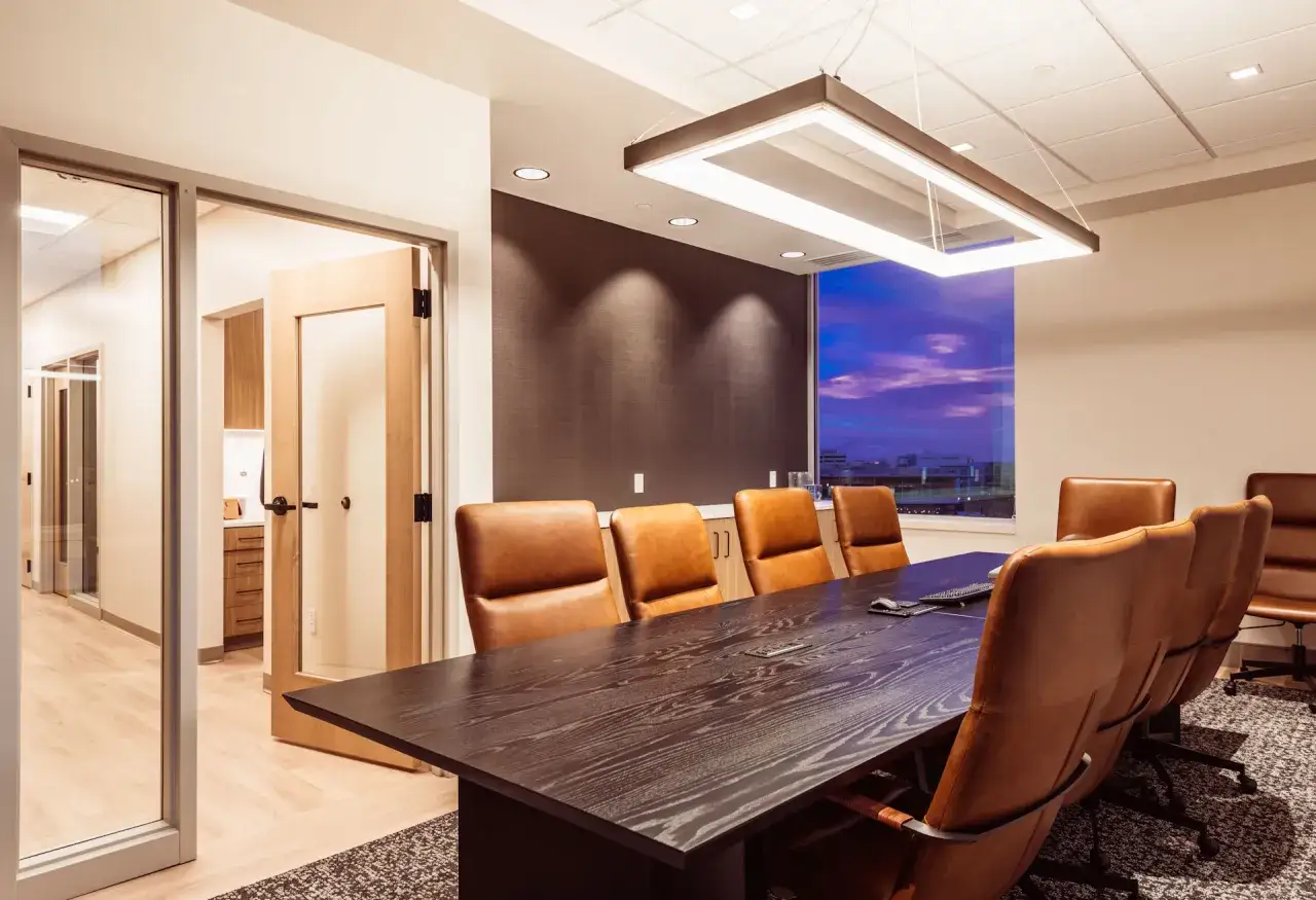 Sala riunioni moderna, parte di un progetto studio medico, con tavolo in legno scuro, sedie in pelle color cuoio e vista panoramica al tramonto.