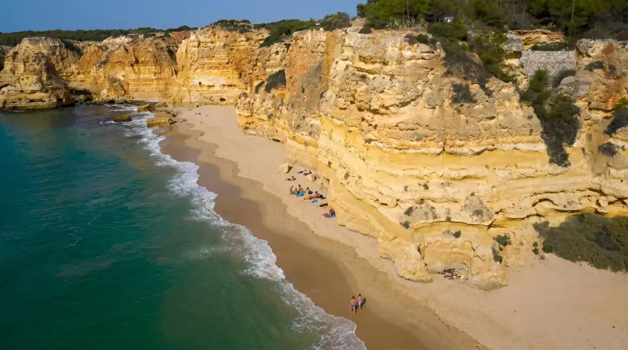Sonne, Sand und Meer an der Praia do Beliche. T&uuml;rkises Wasser umsp&uuml;lt goldene Felsen, w&auml;hrend Urlauber die Ruhe genie&szlig;en.