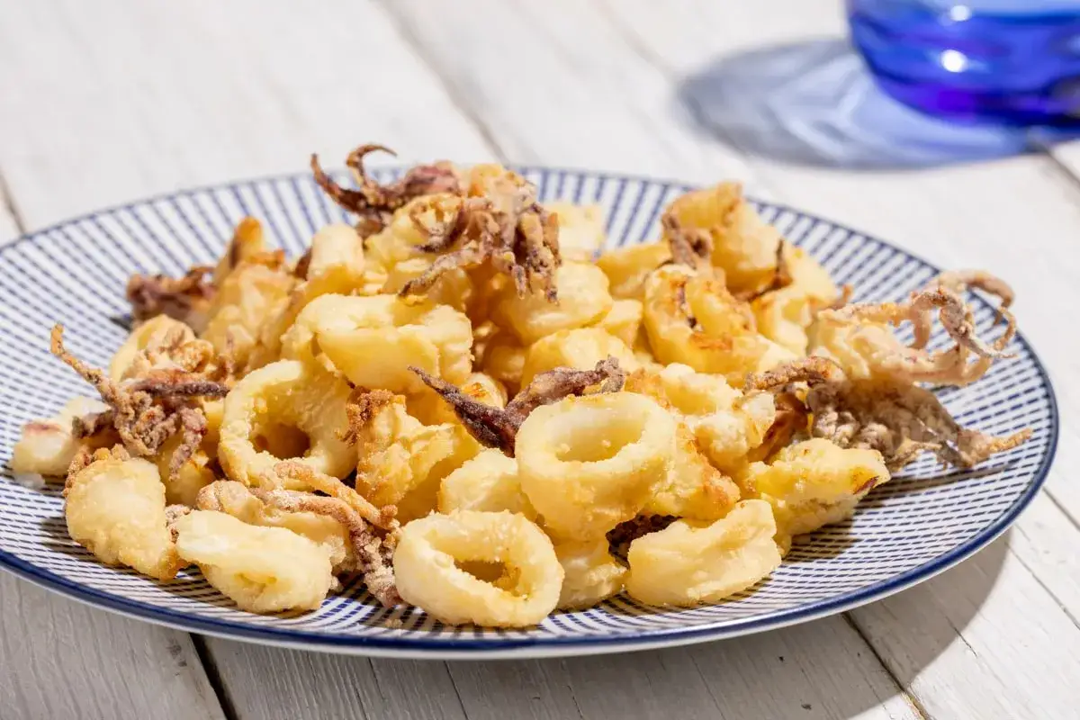 Calamari croccanti e dorati, preparati nella friggitrice ad aria, serviti su un piatto a righe blu.
