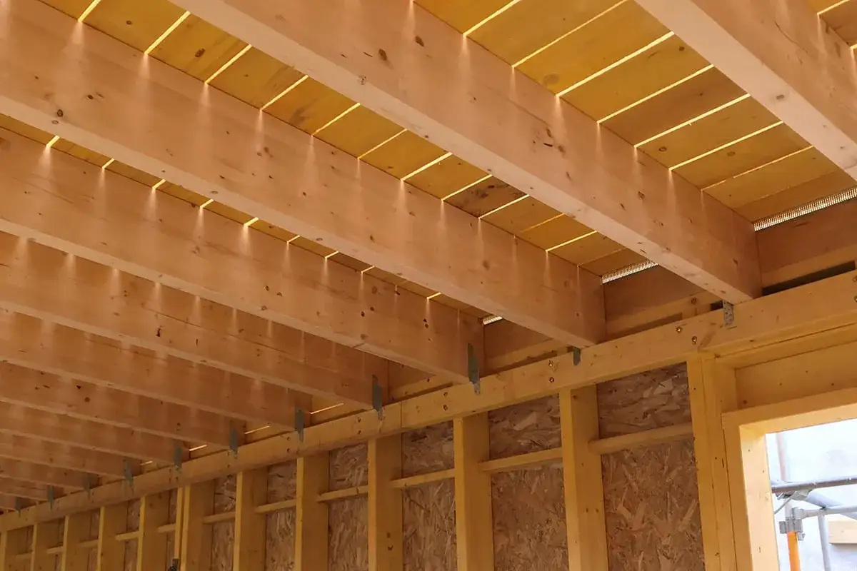 Structure en bois pour refaire un plancher sur poutre. Lumière filtrant entre les solives.