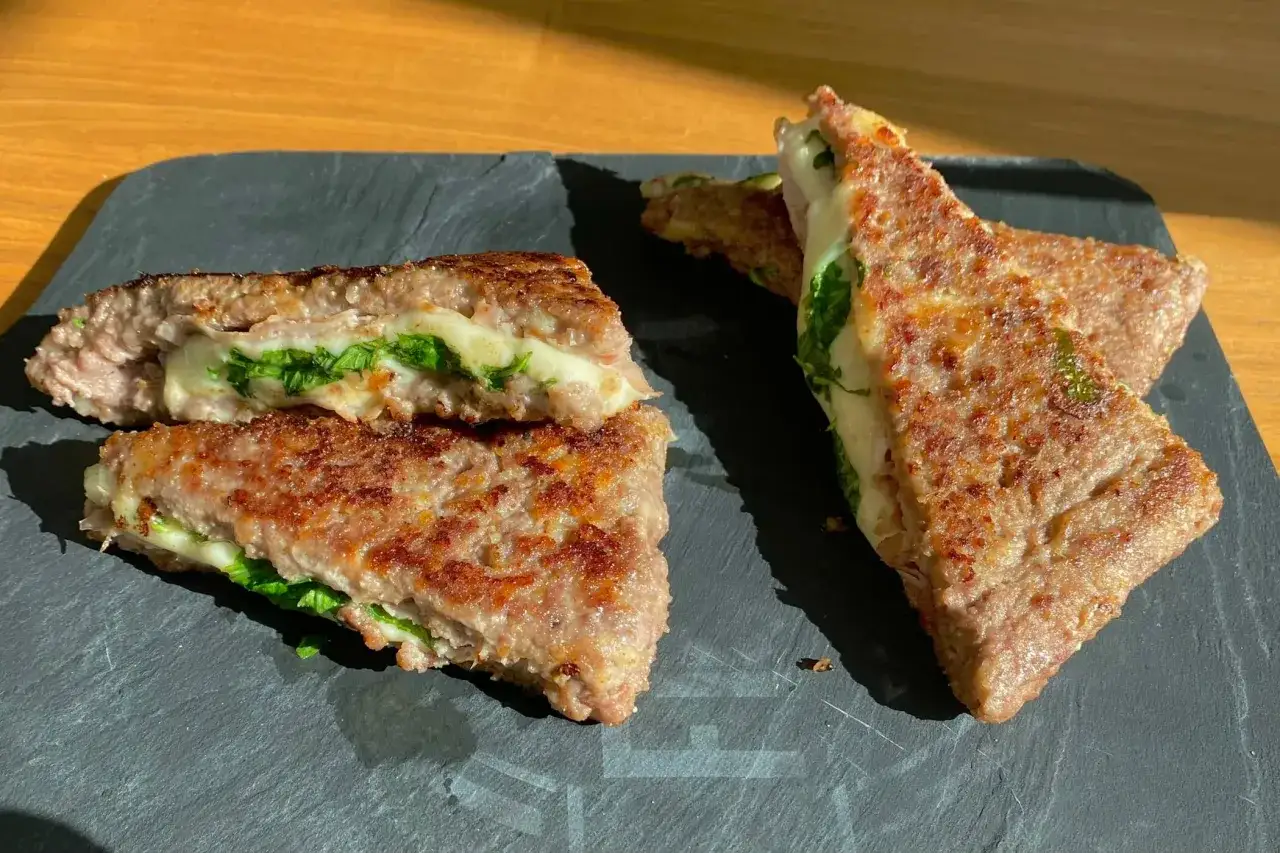 Deliziose ricette con carne macinata: hamburger ripieni di formaggio filante e verdure fresche, serviti su una pietra scura.