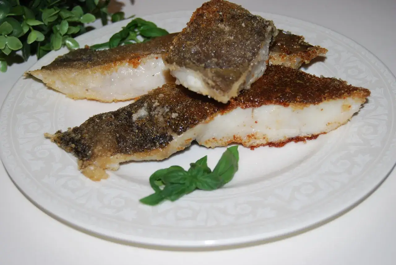 Chrupiący halibut smażony na złoto, podany na białym talerzu z listkami bazylii.