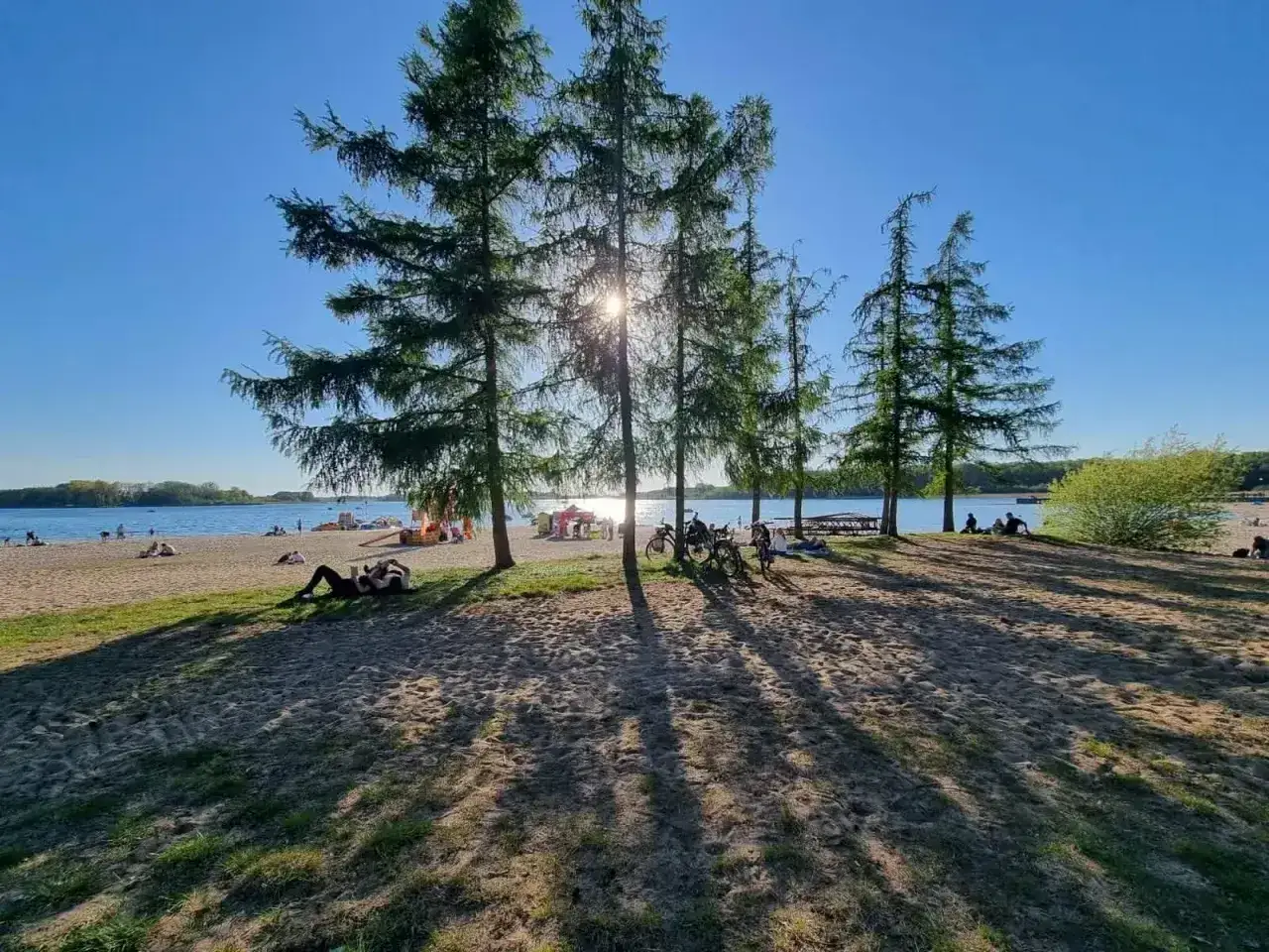 Słoneczna plaża w Skorzęcinie, ludzie odpoczywają pod drzewami, rowery czekają na wycieczkę. Skorzęcin atrakcje to idealne miejsce na relaks.