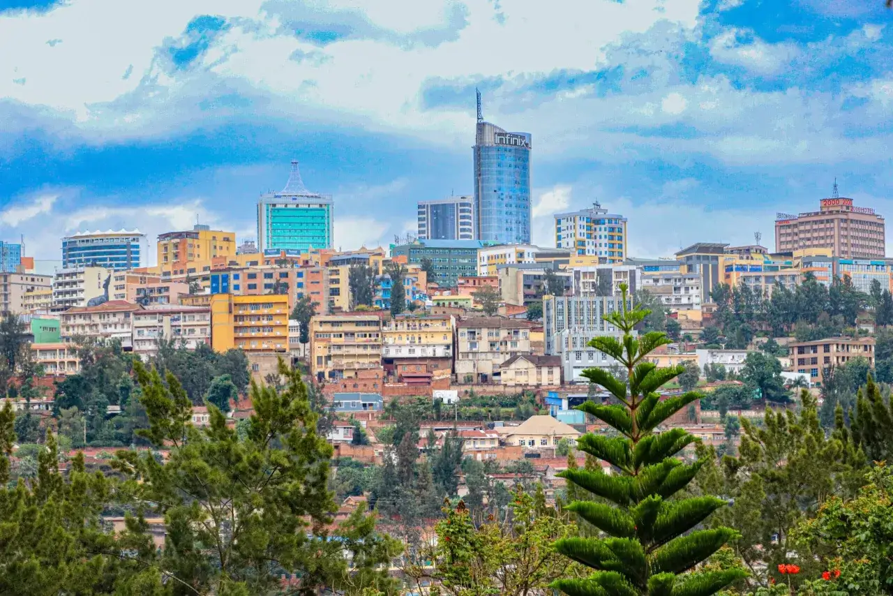 Widok na wzgórza Kigali, Rwanda, z kolorowymi budynkami i wieżowcami na tle błękitnego, chmurnego nieba.
