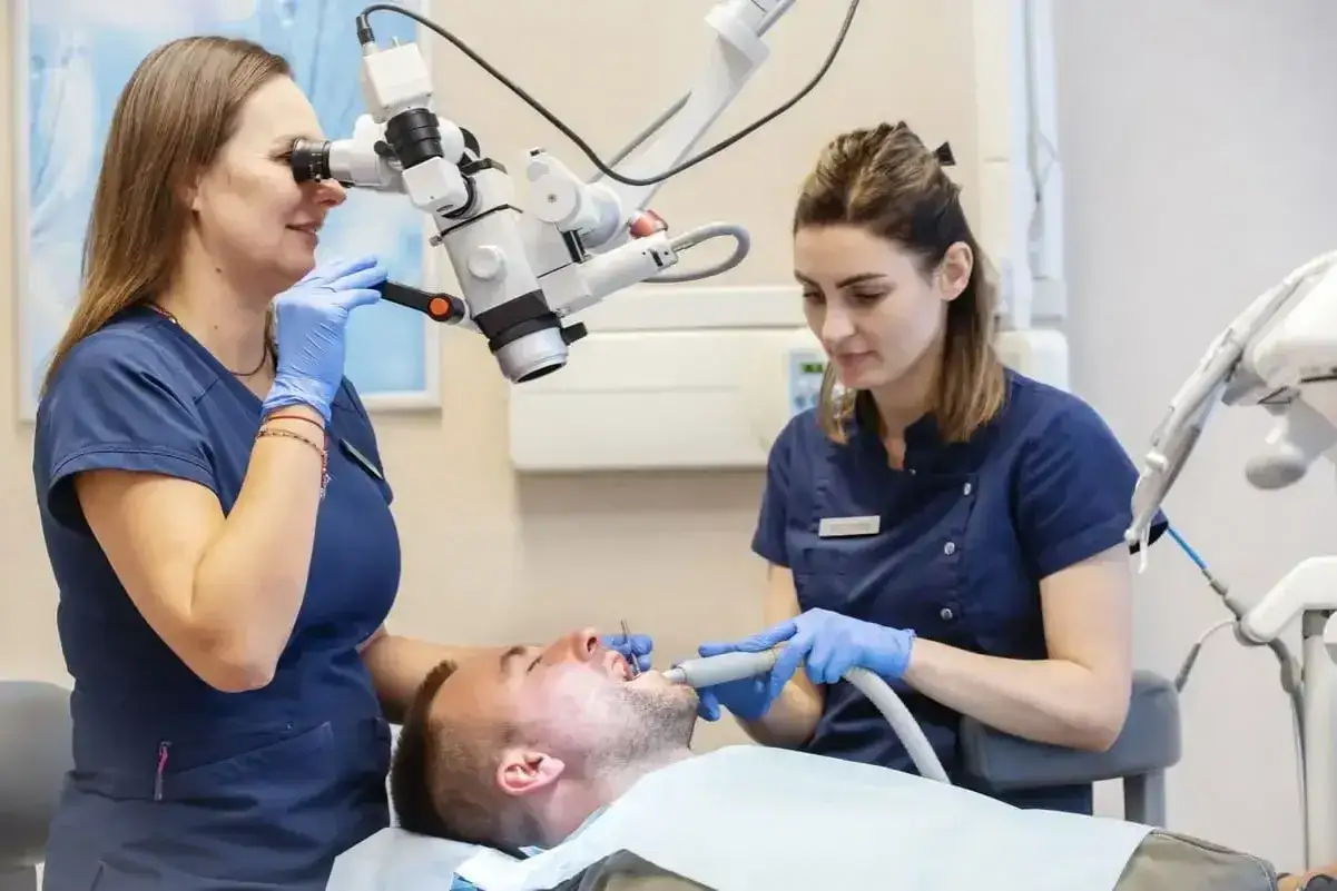 Dentystka z asystentką pracują przy pacjencie. Zastanawiasz się, ile kosztuje znieczulenie u dentysty na NFZ?