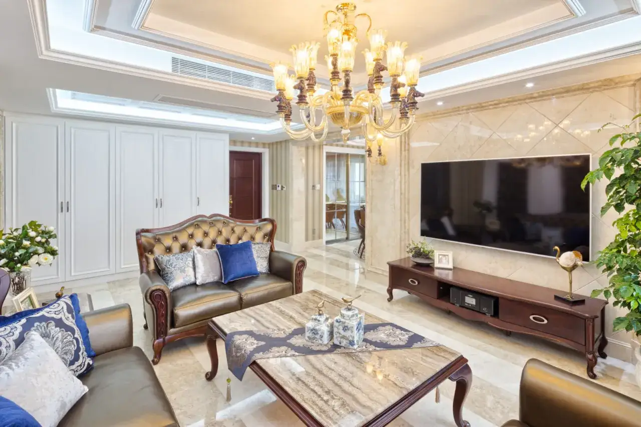 Eleganckie **styl glamour mieszkanie** z brązową sofą, marmurowym stolikiem i kryształowym żyrandolem.