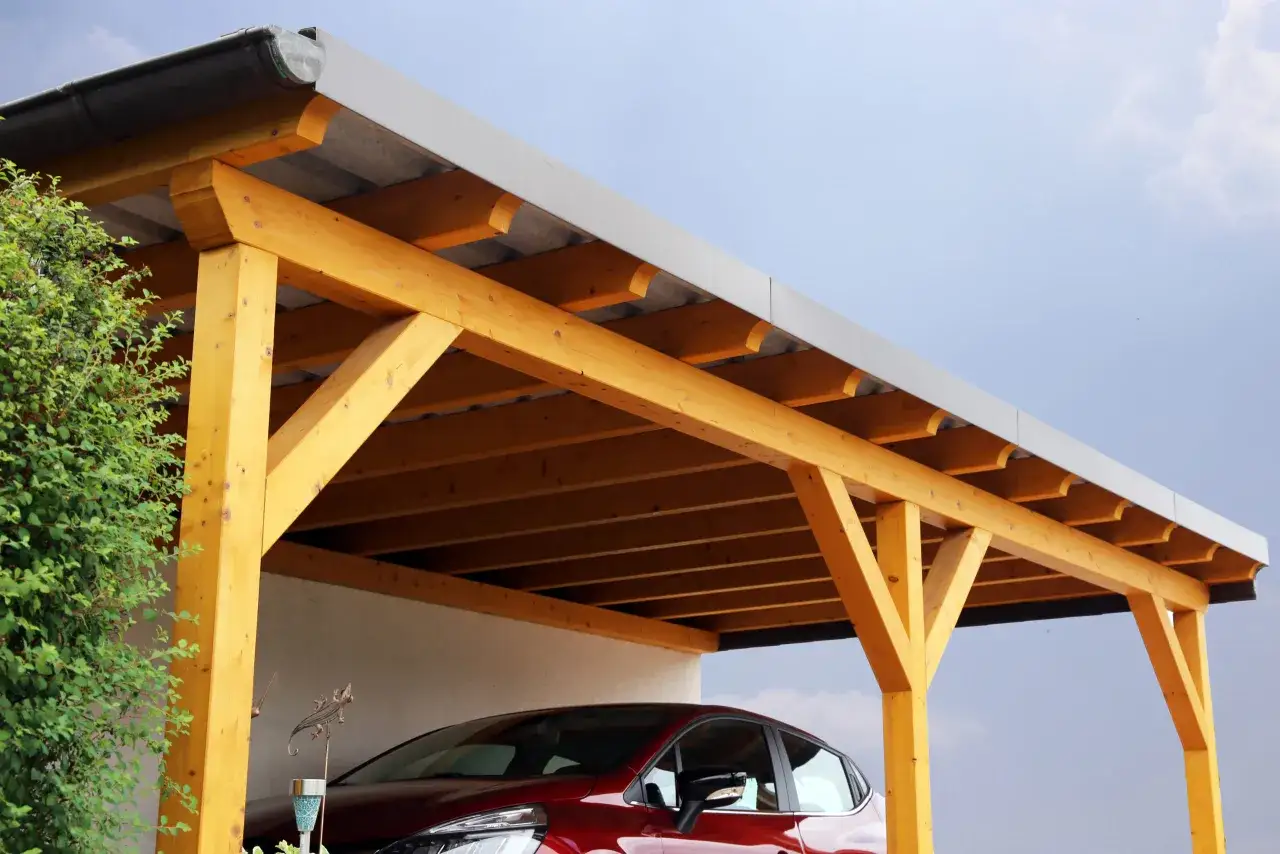 A newly built wooden carport, a great example of how to build a carport, shelters a red car.