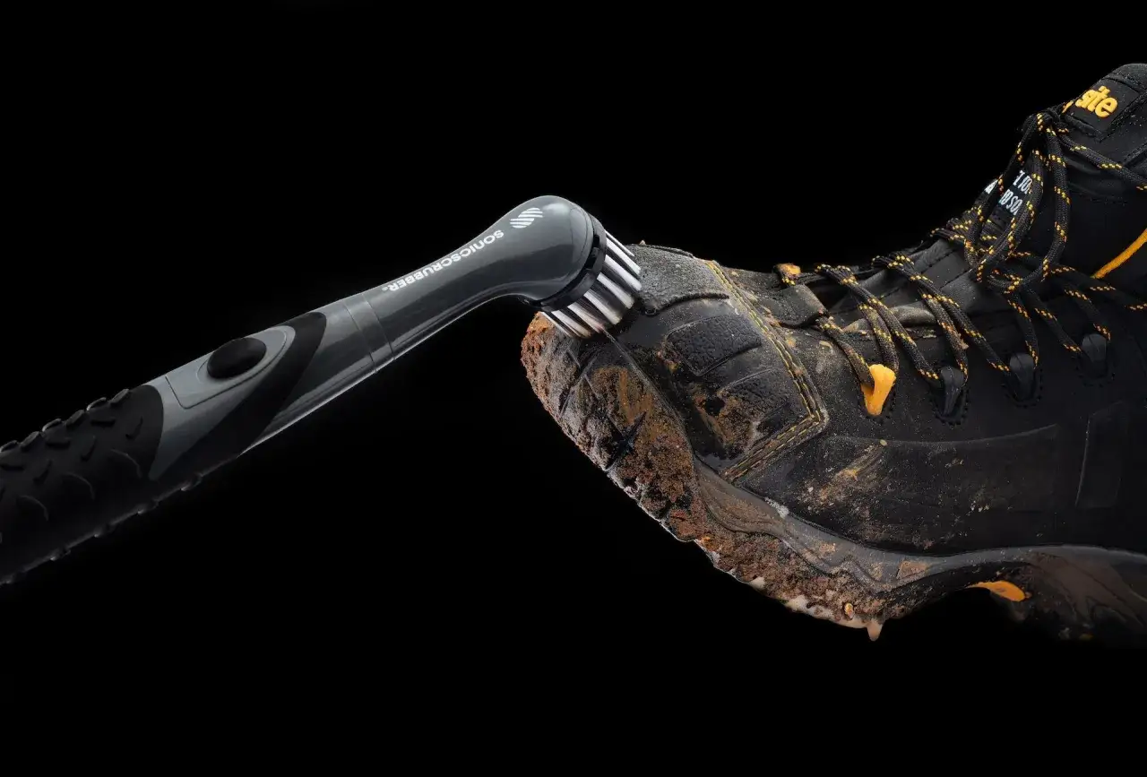 A powered scrubber cleans mud from a work boot, showing how to maintain shoes.