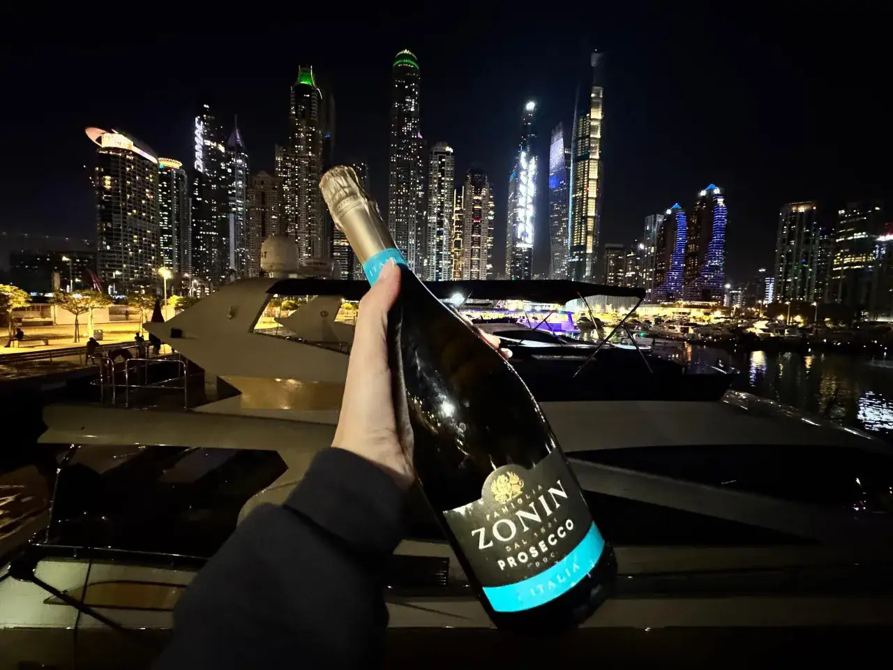 Butelka prosecco na tle nocnego Dubaju z wieżowcami i jachtem. Tak, w Dubaju można pić alkohol w wyznaczonych miejscach.