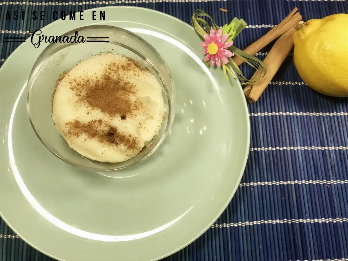Manjar blanco espolvoreado con canela, servido en copa de cristal, junto a lim&oacute;n y canela en rama.