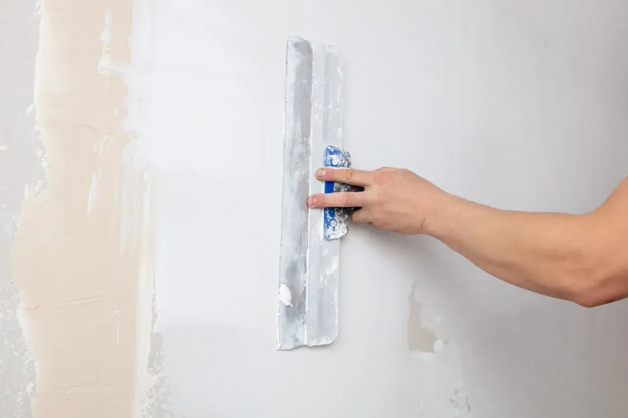 Hand spachtelt eine Wand. Die alte Tapete wird entfernt und die Wand für neue Tapete vorbereitet.