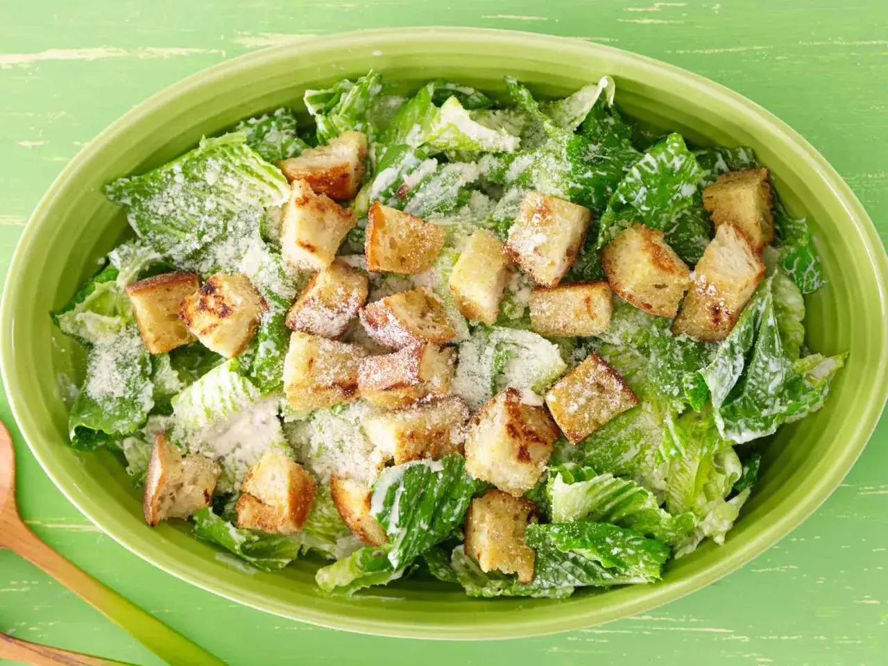 En stor skål med krispig romansallad, krutonger och parmesanost, allt täckt av en krämig caesarsallad dressing.