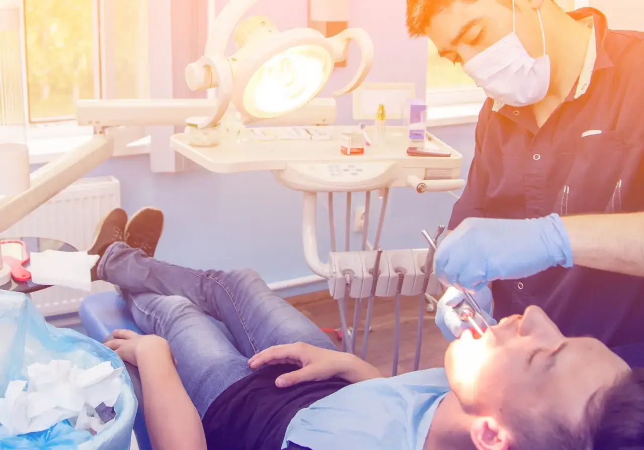 Dentysta wykonuje dłutowanie zęba u pacjenta leżącego na fotelu.