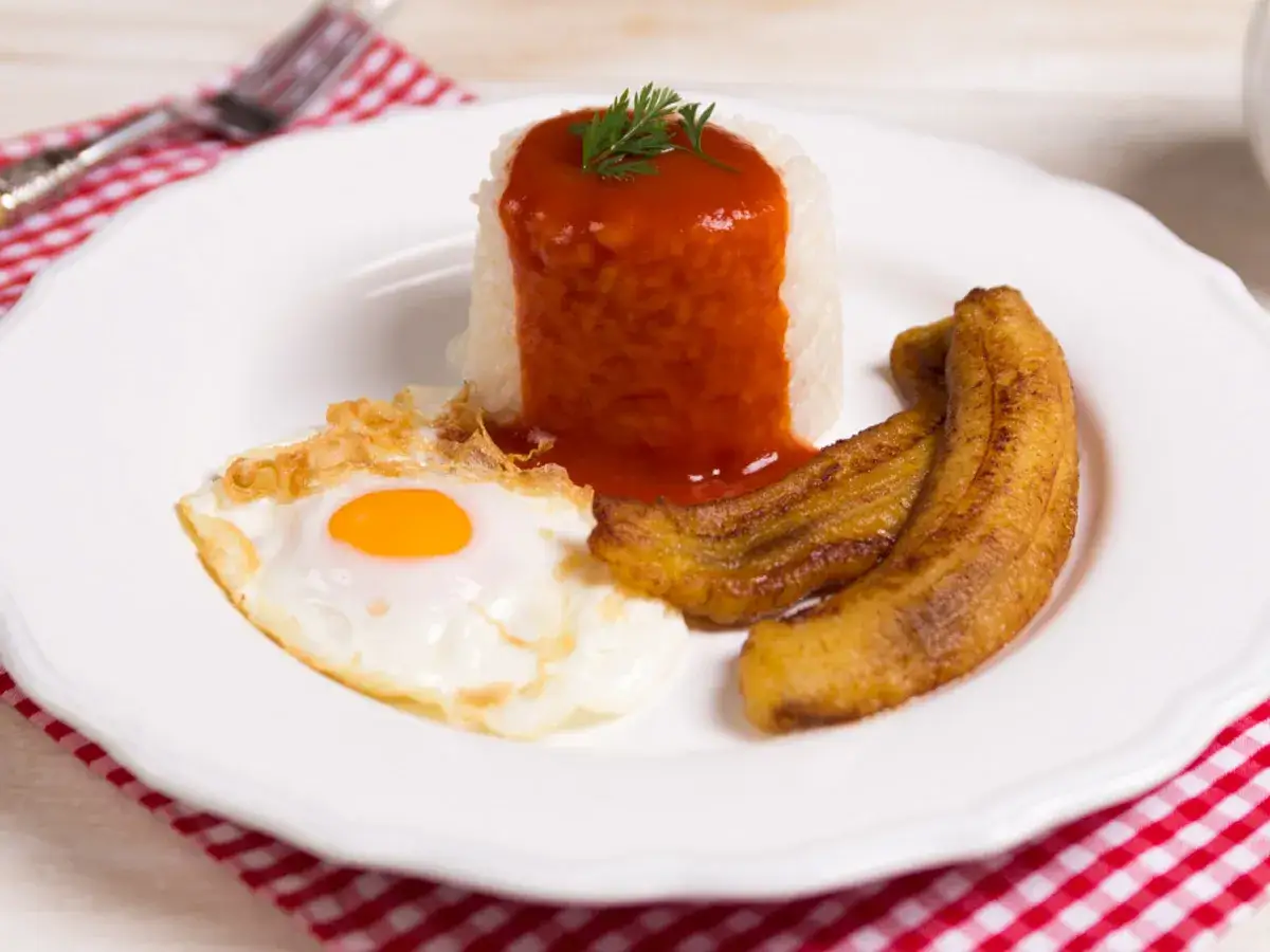Un plato de arroz a la cubana con huevo frito, pl&aacute;tanos maduros fritos y salsa de tomate.