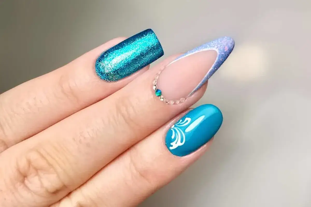 Unghie con glitter blu elettrico, french riviera e decorazioni floreali bianche. Nuove forme unghie audaci e luminose.