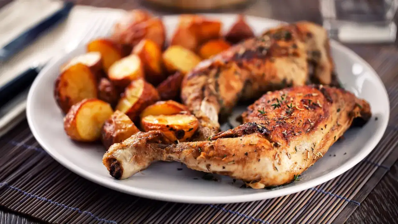 Piatto di pollo al forno dorato e patate arrosto, condito con erbe aromatiche. Un classico sapore casalingo.