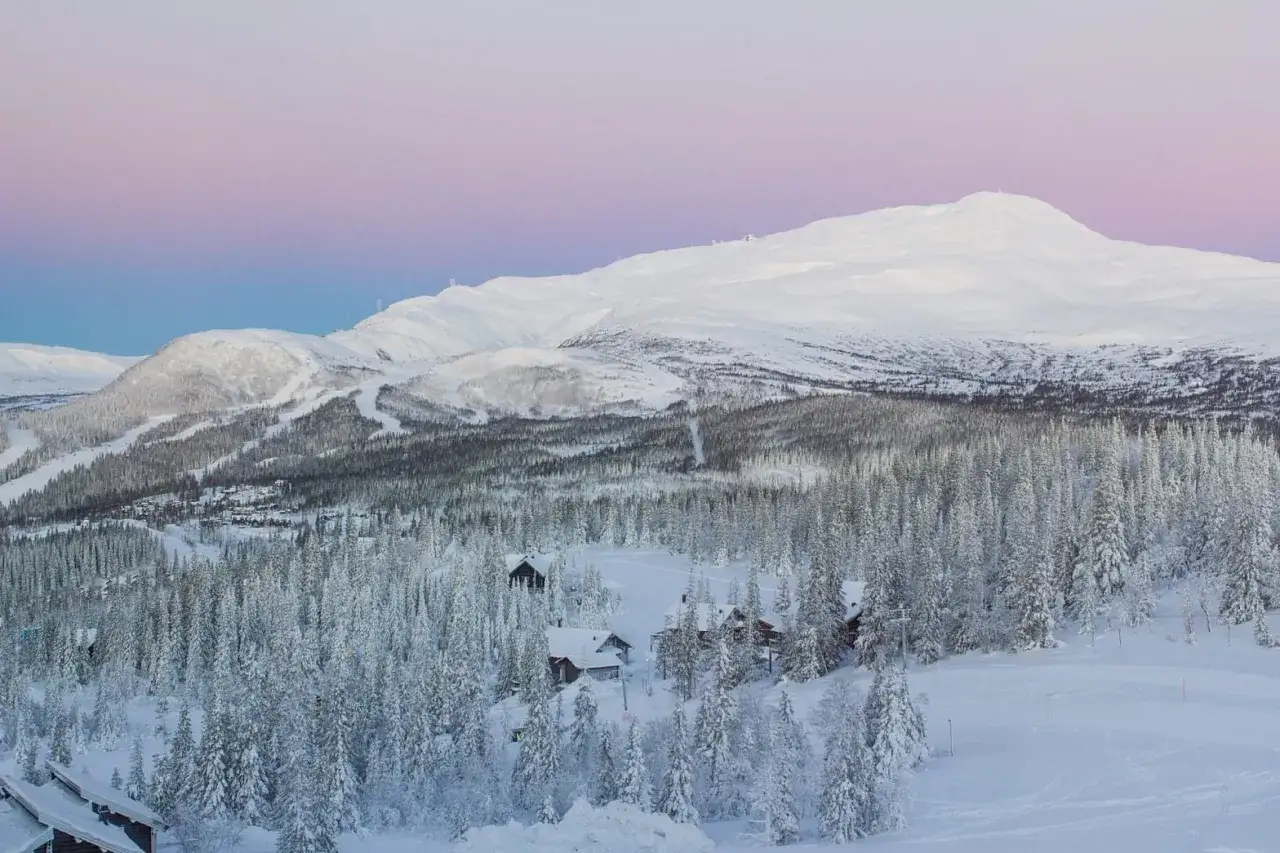 Sn&ouml;t&auml;ckta berg och skogar i Sverige, perfekt f&ouml;r en dag med **downhill sverige**. Solnedg&aring;ngens rosa och bl&aring; toner f&auml;rgar himlen.