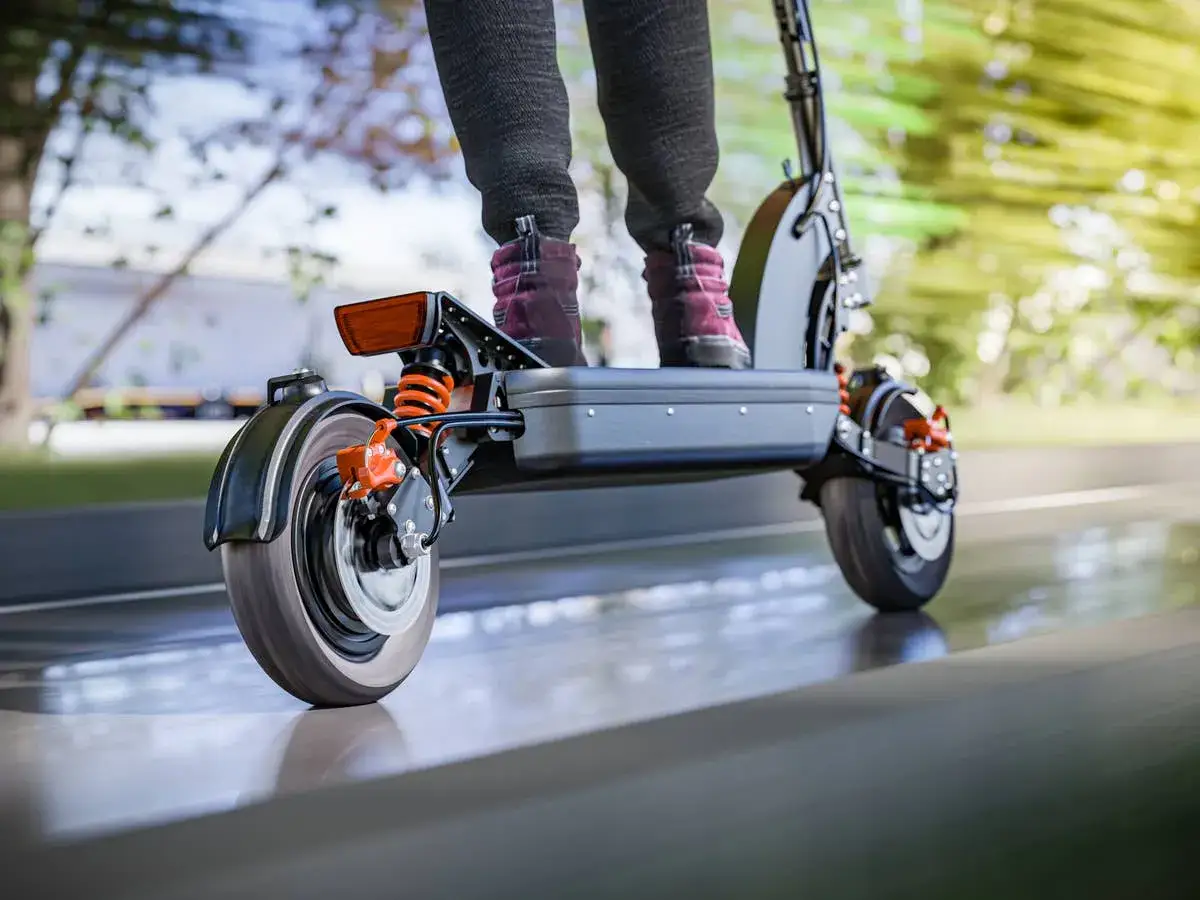Person auf E-Roller im Test, fährt auf Straße. Federung und Bremsen sind gut sichtbar.