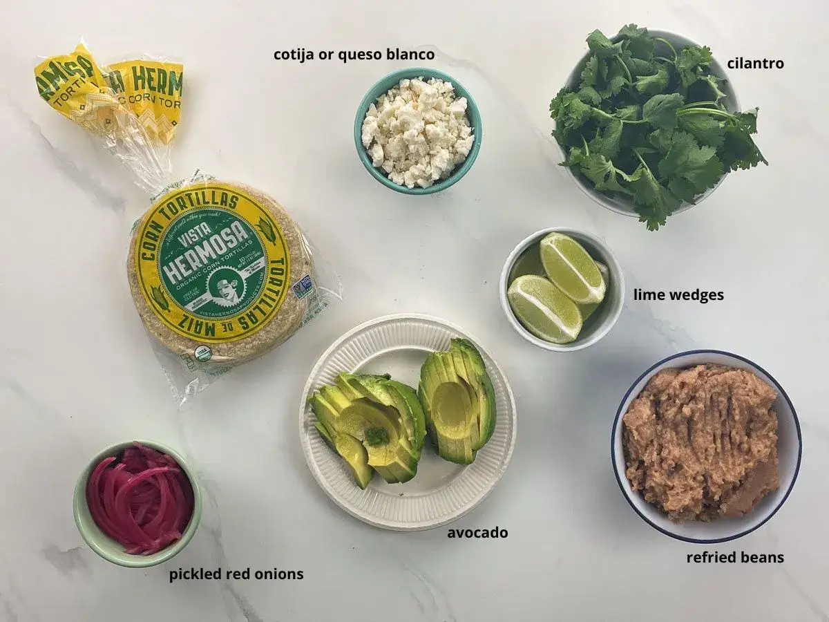 H&auml;r &auml;r ingredienser f&ouml;r tacos: majstortillas, refried beans, avokado, picklad r&ouml;dl&ouml;k, koriander, limeklyftor och cotijaost.