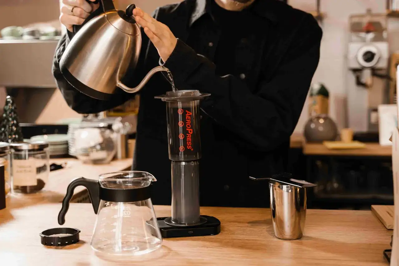 Osoba zalewa gorącą wodą kawę w urządzeniu Aeropress, przygotowując pyszne espresso.
