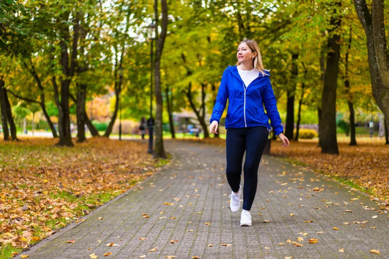 Donna cammina in un parco autunnale, godendosi i benefici della camminata. Foglie dorate coprono il sentiero.