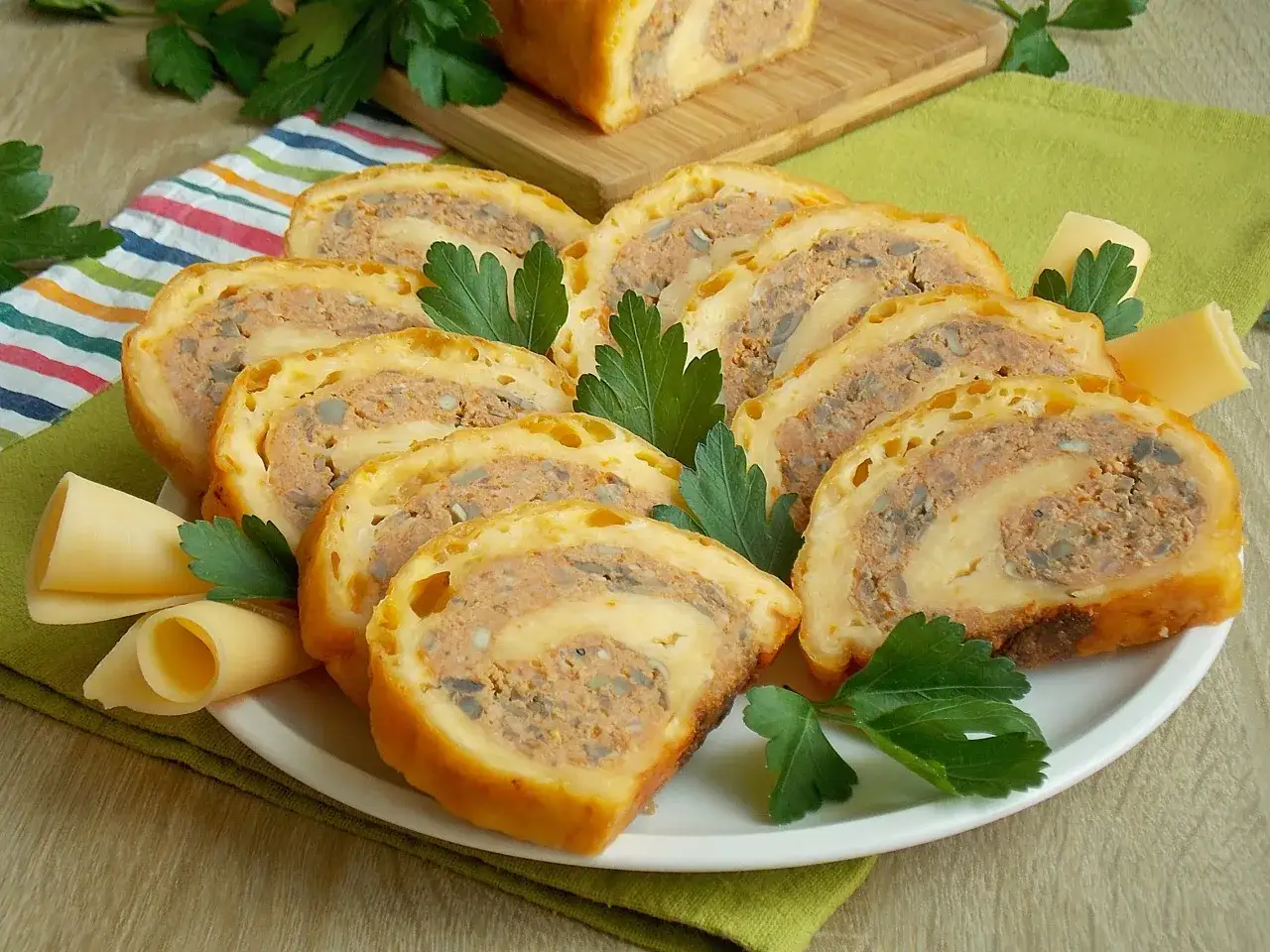Pyszna rolada z mięsa mielonego z pieczarkami, pokrojona w plastry, podana na talerzu z serem i natką pietruszki.
