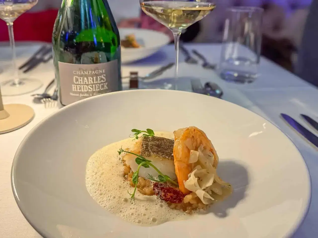 Ein Gourmet-Gericht mit Fisch und Garnelen, serviert mit einem Glas Charles Heidsieck Blanc de Blancs Champagner.