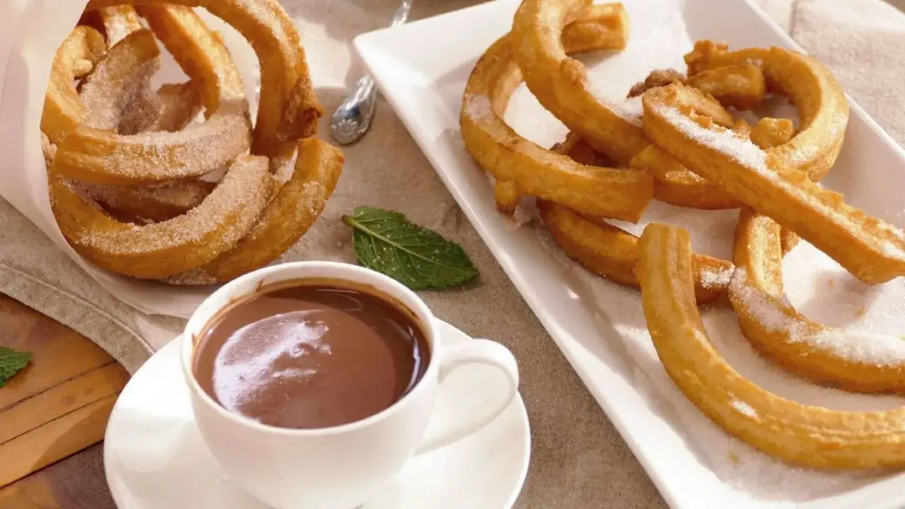 Churros sin gluten espolvoreados con azúcar, servidos con una taza de chocolate caliente.