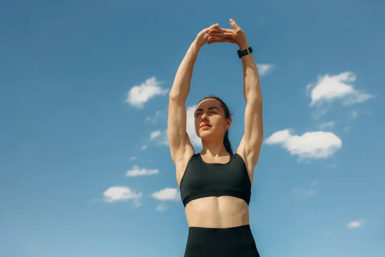 Mujer estirando brazos al cielo, disfrutando de ejercicios de relajaci&oacute;n despu&eacute;s de hacer ejercicio.