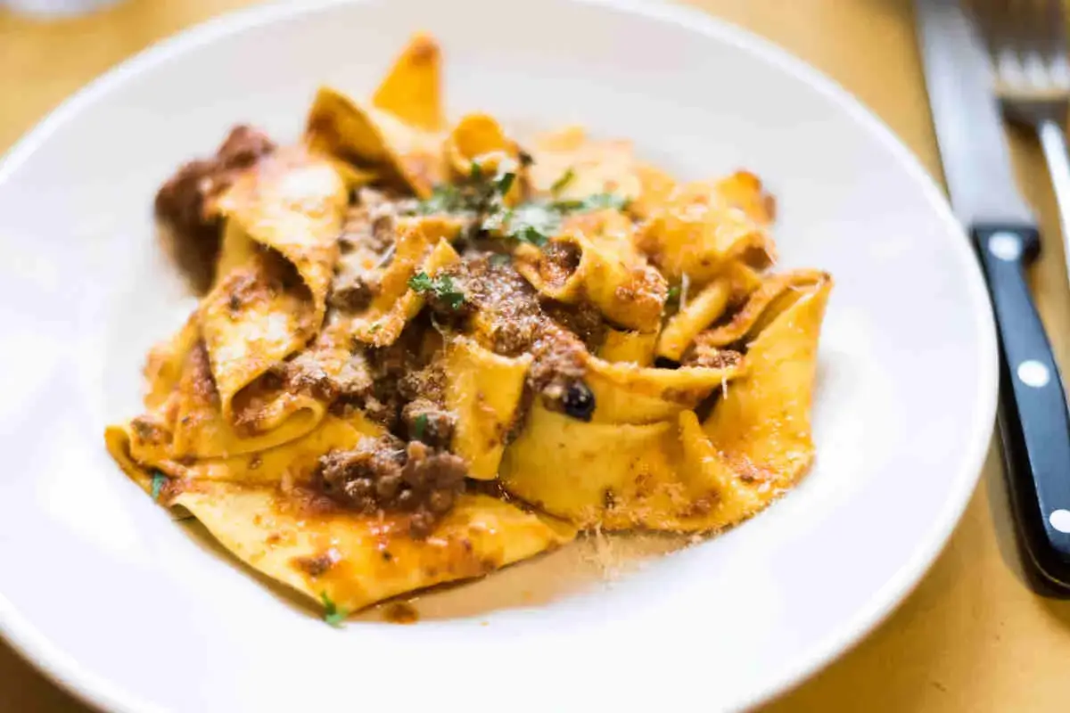 Piatto di pasta fatta in casa con rag&ugrave; ricco e parmigiano grattugiato, pronto per essere gustato.