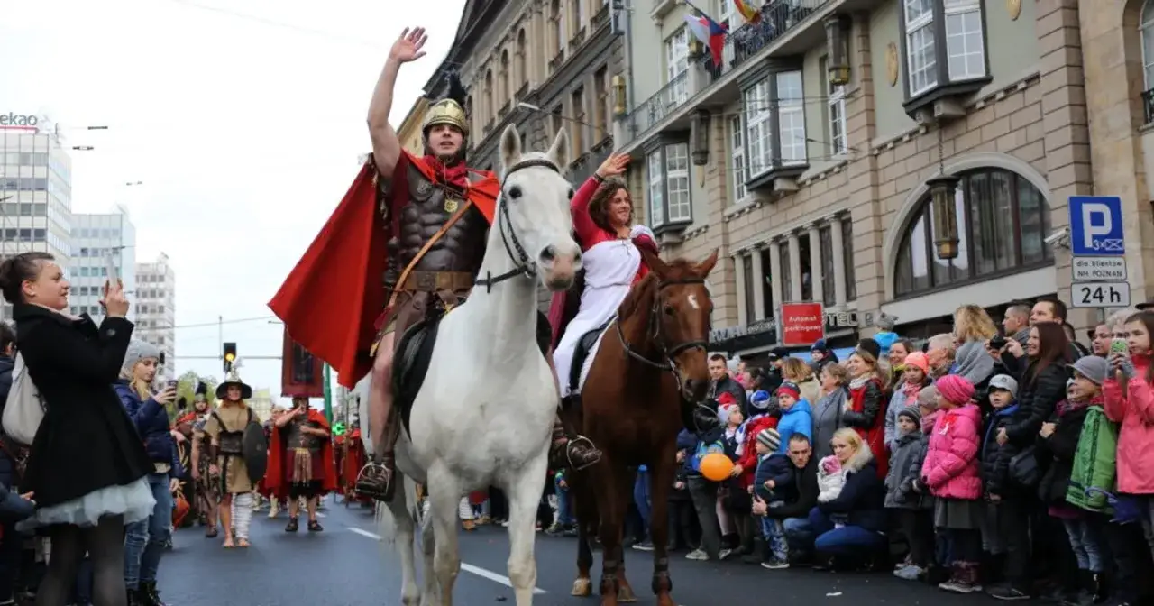Bractwo konne św. Marcina w historycznych strojach przemierza ulicę, pozdrawiając tłum widzów.