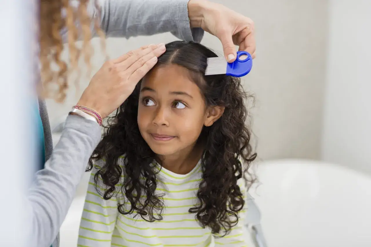 Una mano peina el cabello de una niña con un peine azul, parte del tratamiento piojos niños.