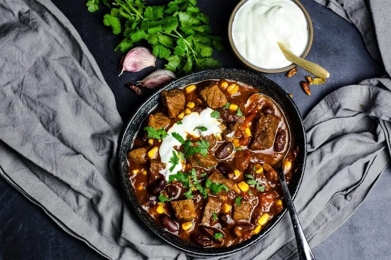 Herzhaftes Chili con Carne mit Rindfleischwürfeln, Bohnen und Mais, garniert mit einem Klecks Sauerrahm und frischem Koriander.