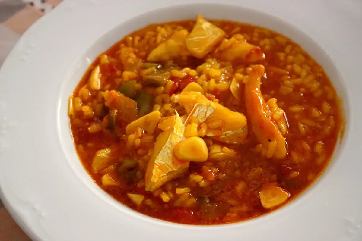 Un plato humeante de arroz con bacalao, con trozos de pescado blanco tierno y verduras en una salsa rojiza.