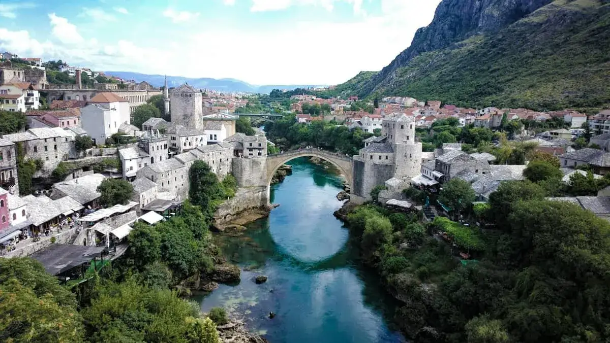 Mostar, Bośnia i Hercegowina: Stary Most nad turkusową rzeką Neretwą, otoczony kamiennymi budynkami i zielenią.