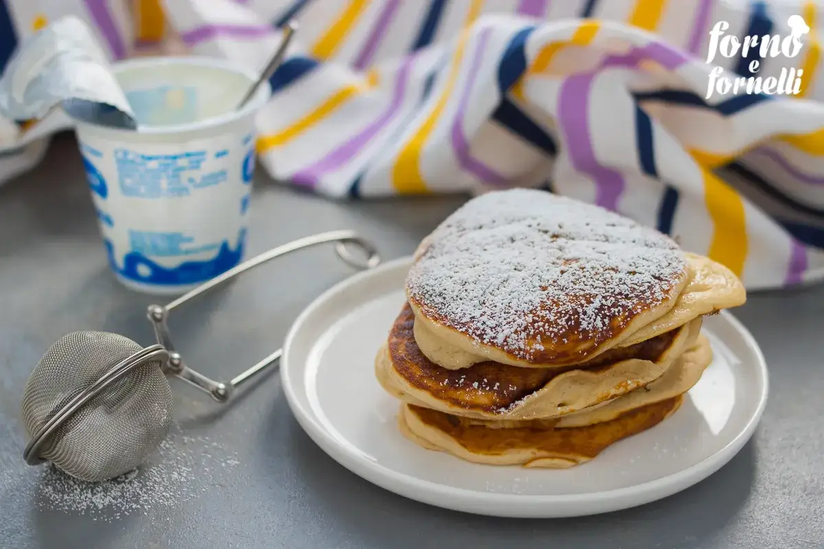 Pancake senza uova con yogurt, spolverati di zucchero a velo, pronti per una colazione leggera.