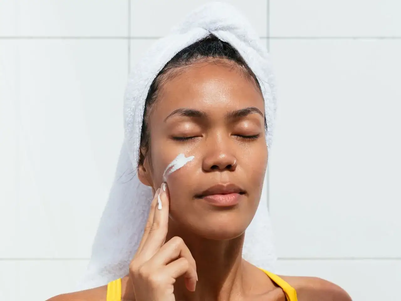 Une femme applique de la crème sur son visage, un geste simple pour savoir comment hydrater sa peau.