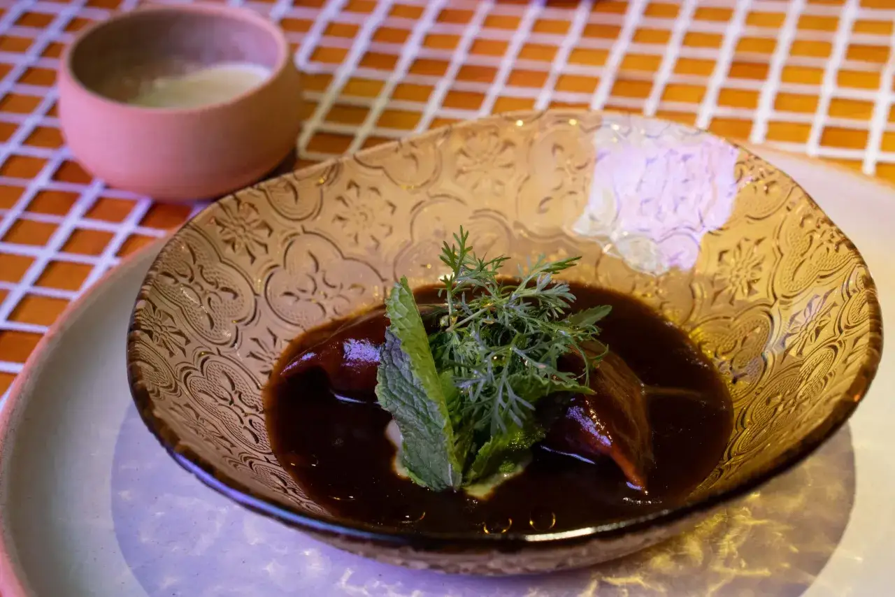 Plato de mole oscuro con hierbas frescas, servido en un cuenco de cristal labrado. ¡Un sabor que te hará decir