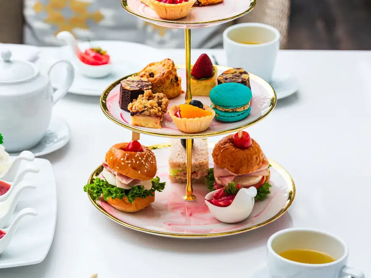 Delicioso pastel de tres niveles con bocadillos, pasteles y macarons, perfecto para la hora del té en Inglaterra.
