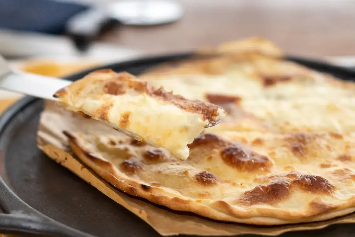 En bit av en gyllene focaccia di Recco med smält ost lyfts från en gjutjärnspanna.